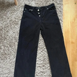 Svarta manchesterbyxor från Samsøe Samsøe - Svarta manchesterbyxor från Samsøe Samsøe!  Byxorna har synliga silverfärgade knappar framtill och klassiska fickor både fram och bak. Snygg, tidlös look med mjukt material och diskret struktur. De är lika korta för min smak på mig som är 165, men helt perfekta om man gillar looken eller är lite kortare!!