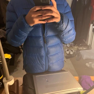 Blå Peak Performance dunjacka M - Säljer en blå dunjacka från Peak Performance i storlek M. Jackan har en snygg puffer-design med horisontella sömmar, huva och dragkedja framtill. Perfekt för kalla dagar och har en clean look med diskret logga på bröstet.