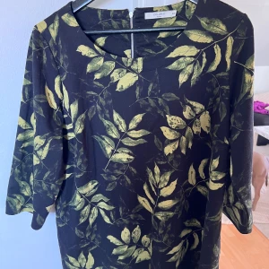 Svart lång tröja med grönt bladprint Cellbes - Svart klänning från Cellbes med grönt bladprint och rund hals. Klänningen har trekvartsärmar och dragkedja bak. Materialet är mjukt och stretchigt, perfekt för dig som gillar naturinspirerade mönster och vill ha en bekväm passform.