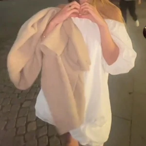 Vit offshoulder kortklänning - Säljer en vit kortklänning med offshoulder-design och puffiga trekvartsärmar. Klänningen har en luftig och avslappnad passform, perfekt för varma dagar. Materialet ser ut att vara bomull eller liknande, vilket gör den skön att bära.