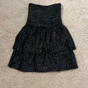 Svart paljettkjol från Gina Tricot - Supersnygg svart kortkjol från Gina Tricot med glittriga paljetter över hela tyget. Kjolen har två lager med volanger.pris kan diskuteras