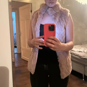 Beige/ljusrosa pälsväst från Mango - Säljer en fluffig och mjuk beige pälsväst från Mango. Västen har en hög krage och är i en loose passform, perfekt att slänga över en hoodie eller långärmad. Materialet är pälsimitation och insidan har ett prickigt foder. Snyggt mönstrad yta med diskreta vågiga linjer. Aldrig använt den och kommer inte till användning för mig ☺️‼️