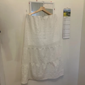 Vit långkjol med volanger - Luftig och flowy vit långkjol med volangdetaljer. Kjolen har en enkel och stilren design med lätt struktur i tyget. Perfekt för en somrig look och passar till många olika toppar. Resår i midjan för extra komfort. Använt en hel del men fortfarande jätte bra kvalité! Små grå fläckar på fram och baksidan som inte har gått bort i tvätten, är dock inte så synliga. Normal i storleken.