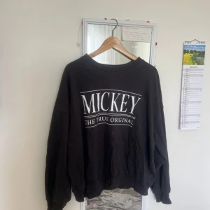 Svart Disney Mickey sweatshirt M - Cool svart sweatshirt från Disney med stort vitt tryck 'MICKEY THE TRUE ORIGINAL' på bröstet. Tröjan har en loose passform och långa ärmar, perfekt för dig som gillar avslappnad stil och ikoniska motiv.
