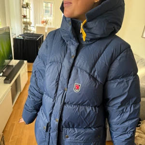 Blå Fjällräven Expedition dunjacka - Säljer en blå Fjällräven Expedition Series dunjacka i storlek WOMENS XL. Passar mig som i vanliga fall bär storlek medium. Jackan har gul snörning i huvan, stora fickor med knappar och dragkedja framtill. Köpt direkt från fjällräven butik. Kvitto finns.