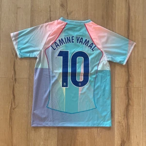 Barça Lamine Yamal Nike fotbollströja M - Säljer en Barcelona fotbollströja med Lamine Yamal och nummer 10 på ryggen. Tröjan har coola pastellfärger i blått, rosa och vitt, med mönstrade detaljer och klubbmärke på bröstet. Nike Dri-Fit material, kortärmad och med Spotify-logga framtill.