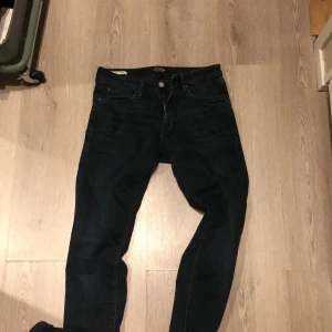 Mörkblå slim jeans med slitningar - Säljer ett par mörkblå jeans med slim passform och snygga slitningar vid knäet. Jeansen har klassisk femficksdesign och är tillverkade i stretchigt denim för skön komfort. Perfekt för dig som gillar en tajt och modern look. Ny pris 1299 mitt pris 379