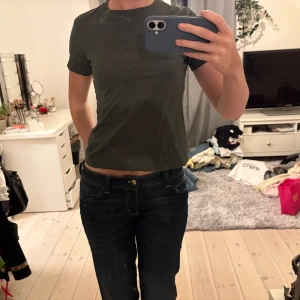 Mörkgrön croppad t-shirt - Säljer en enkel och stilren mörkgrön croppad t-shirt med korta ärmar. Perfekt för dig som gillar en clean look och vill ha något som är lätt att matcha med jeans eller shorts. Materialet känns mjukt och bekvämt mot huden.