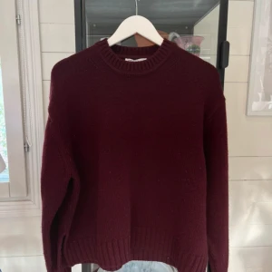 Vinröd stickad tröja från Zara - Snygg vinröd stickad tröja från Zara med rund hals och ribbade muddar vid hals, ärmslut och nederkant. Modellen är loose fit och har långa ärmar, perfekt för att hålla dig varm under kyliga dagar. Enkel och stilren design som är lätt att matcha.