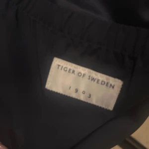 Svart parkajacka från Tiger of Sweden - Svart parkajacka från Tiger of Sweden med fyra stora fickor framtill, snygga tryckknappar och dragkedja. Jackan har en klassisk krage och är perfekt för dig som gillar stilren och funktionell design. Materialet är slitstarkt och jackan har långärmade ärmar.