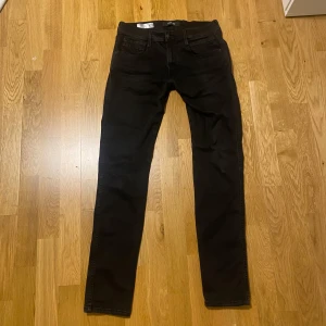 Svarta Replay jeans, midja 32 längd 34 - Svarta jeans från Replay med klassisk femficksdesign och blå Replay-detalj vid fickan. Snygg rak passform och diskret look som funkar till det mesta. Tillverkade i ett mjukt och slitstarkt jeanstyg. Perfekta för dig som gillar stilrena svarta jeans. Hyperflex jeans