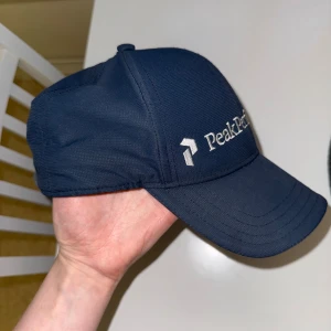 Mörkblå keps Peak Performance L/XL - Snygg mörkblå keps från Peak Performance i modellen Brocket Cap. Kepsen har böjd skärm, justerbar rem bak och broderad logga framtill. Tillverkad i slitstark polyester, perfekt för en sportig och stilren look.