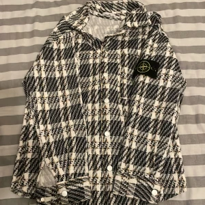 Rutig overshirt från Stone Island - Säljer en fet overshirt från Stone Island med svart, vit och gul rutig design. Skjortan har klassisk krage, långa ärmar och snygga knappar framtill. Materialet är grovt och känns riktigt lyxigt. Ikonisk Stone Island patch på ärmen för extra street cred.