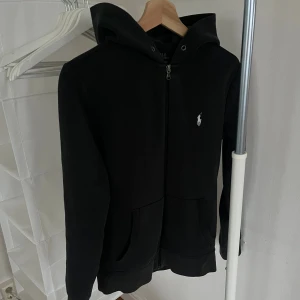Svart hoodie från Polo Ralph Lauren - Svart hoodie från Polo Ralph Lauren. En riktig snygg och bekväm hoodie. Snörerna har dragits ut men har de vid sidan av om man vill ha de. Hoodien är i storlek xs. Hör gärna av dig om du har några funderingar 