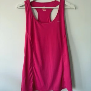 Rosa linnetopp från Puma i XL - Sportig och snygg rosa linnetopp från Puma i storlek XL. Toppen har en klassisk racerback och är tillverkad i mjuk polyester som andas. Perfekt för träning eller när du vill ha en bekväm och färgstark look. Diskret Puma-logga på bröstet.