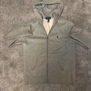 Grå hoodie från Polo Ralph Lauren - Säljer en stilren grå hoodie från Polo Ralph Lauren med dragkedja och huva. Den är nästan helt oanvänd och personen på bilden är 178. Den sitter litet, passar nog mellan 160-170