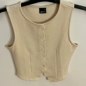 Beige väst med knappar från Gina Tricot - Snygg beige väst från Gina Tricot i storlek XS. Nästan aldrig använd. Skit snygg att styla tillsammans med något som ex en skjorta