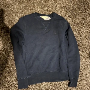 Mörkblå sweatshirt från Burberry XS - Snygg mörkblå sweatshirt från Burberry i storlek XS. Tröjan har rund hals, lång ärm och ett diskret broderat Burberry-logomärke på bröstet. Tillverkad i mjuk bomull och polyesterblandning, perfekt för chill dagar. Klassisk och stilren design.