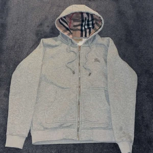 Grå Burberry hoodie - Grå hoodie från Burberry med klassiskt rutigt foder i huvan och längs insidan. Priset kan diskuteras 