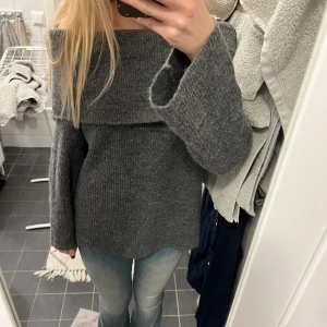 Mörkgrå offshoulder stickad tröja - Säljer en mörkgrå stickad tröja med offshoulder-design och bred krage. Tröjan har långärmade, lite vidare ärmar och är ribbstickad för en snygg struktur. Perfekt för dig som gillar en chill och trendig look.