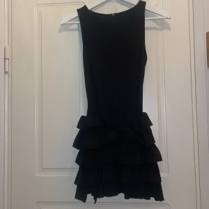 Svart volangklänning från SHEIN XS - Supersnygg svart kortklänning från SHEIN i storlek XS. Klänningen är ärmlös och har flera lager med volanger nedtill som ger en cool och lekfull look. Perfekt för dig som gillar att sticka ut med detaljer och gillar en tight passform. Den har en slags insydd shorts under klänningen.