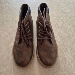 Skor - Bruna skor från Nautica med snörning och rund tå. Skorna har en ovandel i syntetmaterial och detaljer i brunt tyg vid hälen. Sulan är i gummi och ger en snygg kontrast till det bruna. Perfekta för dig som gillar en clean och stilren look.