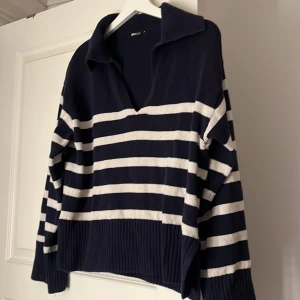 Randig stickad tröja  - Mörkblå och vit stickad tröja från Gina Tricot i storlek S. Tröjan har breda ränder, v-ringad krage och ribbade muddar samt slits i sidorna. Perfekt för dig som gillar en chill och snygg look med lite preppy vibe.