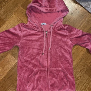 Rosa velour hoodie med dragkedja XS - Mjuk och chill rosa hoodie i velour från C, storlek XS. Tröjan har huva med snörning, dragkedja framtill och två fickor. Perfekt för dig som gillar comfy vibes och vill ha något som sticker ut lite med sin glansiga look.