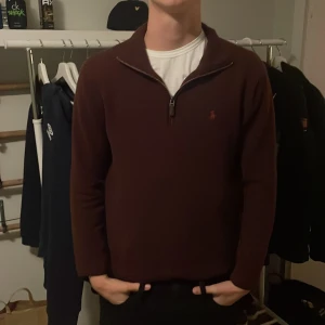 Vinröd half zip tröja Polo Ralph Lauren - Snygg vinröd långärmad tröja från Polo Ralph Lauren med half zip och liten broderad logga på bröstet. Tröjan har en klassisk krage och är gjord i mjuk bomull, perfekt för chill höst- och vinterdagar. Passar dig som gillar stilren och enkel design.