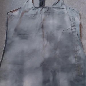 Grå linnetopp från Better Bodies - Säljer en grå linnetopp från Better Bodies med racerback och diskret logga längs sidan. Toppen har en snygg, lite mönstrad effekt i tyget. Perfekt för dig som gillar sportig stil och vill ha något bekvämt till gymmet.