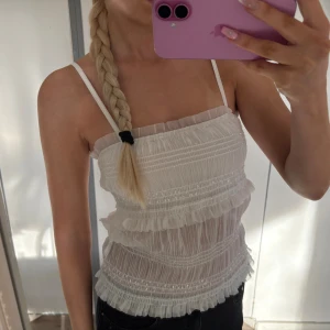 Vit volangig linnetopp med smala band - Söt lite glittrig vit linnetopp med smala axelband och flera volangdetaljer. Perfekt för sommar eller utomlands ☀️
