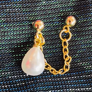 By prisförslag- 1 st Guldörhänge med kedja och pärla - Unikt örhänge med två guldfärgade pluppar, sammankopplade med en tunn kedja i guldton. Ena sidan har en droppformad vit pärla som hänger snyggt och ger en cool vibe. Perfekt för dig som gillar statement-smycken med lite edge.