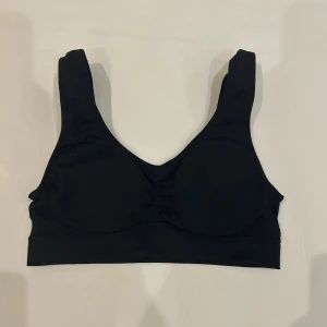 Svart sporttopp L/XL - Svart, träningstopp i stretchigt material med breda axelband och lätt rynkdetalj framtill. Tillverkad i 90% polyamid och 10% elastan för en bekväm och följsam passform. Perfekt för träning eller chill dagar.