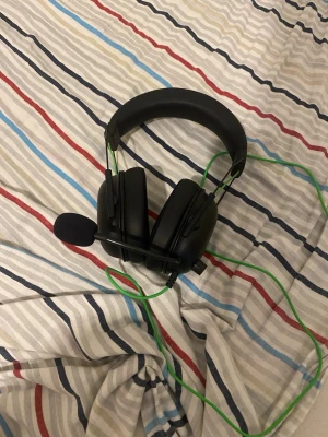Razer BlackShark V2 - Razer BlackShark V2 gaming headset med kabelanslutning och mikrofon. Svart design med gröna detaljer, over-ear-kåpor och justerbar mikrofon. Ser ut att vara i gott skick utan synligt slitage. Perfekt för gaming och kommunikation.