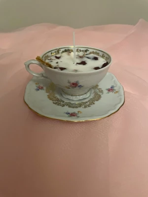 Doftljus i en vit tekopp med blommor i doft utav vanilj nr 5 - Det här ljuset är gjort av återanvändbara material. Tekoppen är köpt secondhand och stearinet är från kyrkor som tänkte slänga det. Det här ljuset har en svag doft utav vanilj, så känsliga även kan använda det. Det här ljuset har även torkade blommor och torkad apelsin på som dekoration. Det finns fler av denna design på hemsidan om man vill köpa sets. 