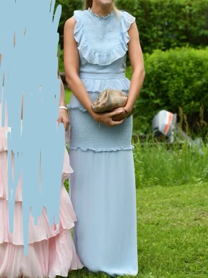 Ljusblå långklänning med volanger - Superfin ljusblå långklänning från märket True Decadence med volanger och smockdetaljer. Klänningen är ärmlös och har flera lager volanger både upptill och i midjan. Storlek 8, passar mig som brukar ha S!