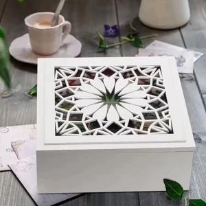 Vit tebox med dekorativt oretalidl  lock i glas  - Snygg tebox i vit trä med ett lock som har ett detaljerat, geometriskt mönster i laser-cut design. Boxen har nio fack för att organisera olika tesorter och mäter 24x24 cm. Perfekt för att hålla koll på dina tepåsar och ge köket en stilren touch. Kontakta mig gärna innan köp. Tack 