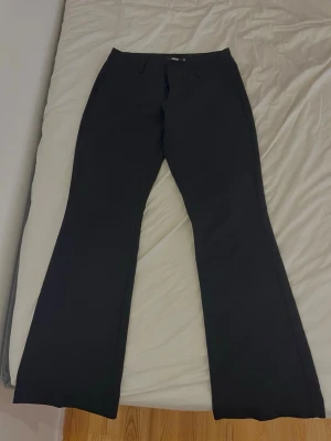Svarta bootcut kostymbyxor Bik Bok lowaisted - Säljer ett par svarta lowaisted kostymbyxor från Bik Bok i storlek 38. Byxorna har bootcut-modell med utsvängda ben och bälteshällor i midjan. Klassisk look som passar till många olika stilar. Materialet känns mjukt och följsamt.