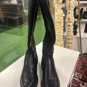 Svarta stövlar från Tamaris - Säljer ett par svarta stövlar från Tamaris med rund tå och platt sula. Skorna har en kombination av slätt skinn och textil med meshpaneler på sidorna samt dragkedja på insidan för enkel på- och avtagning. Perfekt för dig som gillar stilrena och praktiska boots.