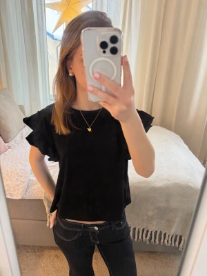 Svart volangtopp  - En svart topp från Zara med volangdetaljer på ärmarna. Modellen är rak, med rund halsringning och korta ärmar. Tryck gärna på köp nu!❤️