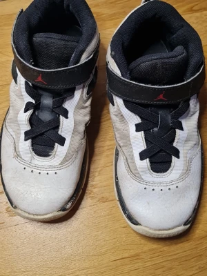  Nike Jordan sneakers svart/vit barn - Säljer ett par Nike Jordan sneakers i svart och vitt med klassisk Jumpman-logga på kardborrebandet. Skorna har snörning, rund tå och är tillverkade i en mix av skinn och textil. Perfekta för dig som gillar sportig stil och streetwear.