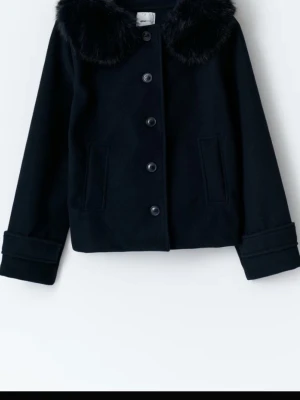 Svart ulljacka med fuskpäls - Snygg svart jacka i ull med krage i fuskpäls och raka ärmar. Klassisk design med knappar framtill och två fickor. Perfekt för dig som vill ha en stilren och varm jacka till hösten eller vintern. Inte allas använd och prislapp kvar