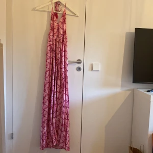 Rosa långklänning från Mango  - Snygg långklänning från Mango i rosa och rött mönster. Klänningen har halterneck med knytband och tofsar, v-ringad front och ett flowigt fall. Helt ny med lapp🩷