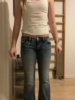 Blå bootcut jeans Gina Tricot 146 - Säljer ett par blå bootcut jeans från Gina Tricot i storlek 146. Jeansen har låg midja, klassiska fem fickor och snygg tvätt med ljusare partier framtill. Tillverkade i jeansmaterial med en skön passform och lätt utsvängda ben.