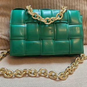 Grön quiltad axelväska med kedja - Säljer en grön axelväska (Bottega V.)  med chunky guldfärgad kedja. Väskan har en cool quiltad design med stora, vadderade rutor och är tillverkad i glansigt skinn. Perfekt för dig som vill sticka ut med en färgstark accessoar. Köparen betalar frakten. 
