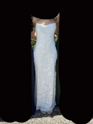 Vit långklänning med spetsdetaljer - Elegant vit långklänning med tunna axelband och vacker spets över hela klänningen. Figurnära passform och lätt utsvängd nertill. Perfekt för student eller bal. Klänningen har en mjuk, romantisk look och subtila blommönster i spetsen. Endast använd en gång, tror att den är i strl XS, men ska dubbelkolla. Funkar bra till middagar, bal, midsommar osv🥰