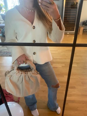 Beige handväska  - Säljer en beige axelväska i mjukt skinn med puffigt handtag och justerbar axelrem. Väskan har en rundad form och rynkade detaljer upptill som ger en trendig look. Perfekt storlek för att få plats med allt du behöver och passar till många olika outfits.