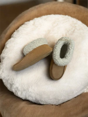 Beiga mockatofflor med ullfoder - Mysiga tofflor i beige mocka med fluffigt vitt ullfoder runt öppningen. De har en klassisk, rundad form och synliga sömmar längs ovansidan. Perfekta för att hålla fötterna varma under kyliga dagar.