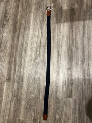 Mörkblå flätad bälte från Jack & Jones - Snyggt mörkblått flätat bälte från Jack & Jones med detaljer i brunt skinn och silverfärgat spänne. Perfekt accessoar för att lyfta din outfit med en klassisk touch. Bältet har en stilren design och passar till både jeans och chinos.