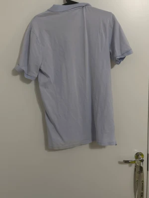 Ljuslila pikétröja från Nike - Säljer en ljuslila pikétröja från Nike med klassisk krage och korta ärmar. Tröjan har vit Nike-logga broderad på bröstet och knappar vid halsen. Perfekt för dig som gillar sportig och stilren look.